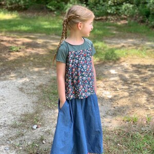May include: A young person wearing a floral print top with a green bodice and a denim skirt with pockets.