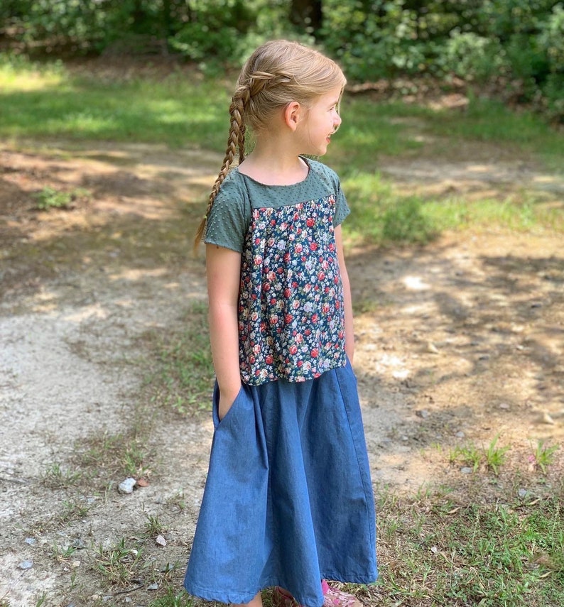 May include: A young person wearing a floral print top with a green bodice and a denim skirt with pockets.