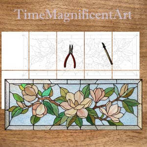 Könnte beinhalten: Ein Buntglasfenster mit einem Magnolienblumendesign mit rosa und cremefarbenen Blütenblättern, grünen Blättern und einem hellblauen Hintergrund. Das Panel ist von einem dunklen Rahmen umgeben. Enthält ein Diagramm und Werkzeuge.