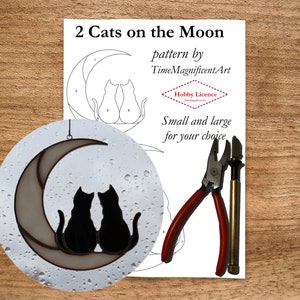 May include: A stained glass pattern of two cats sitting on a crescent moon. The pattern is printed on white paper with the title "2 Cats on the Moon" and the text "pattern by TimeMagnificentArt" and "Hobby Licence". The image also shows a pair of red pliers and a soldering iron.