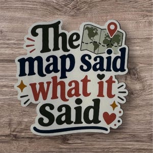 May include: A die-cut sticker featuring the text The map said what it Said in black and red lettering. The design includes a small illustration of a world map with a red location pin, a black heart, and two small four-pointed gold stars.