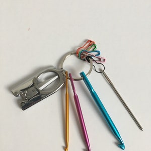May include: A set of colorful crochet hooks and a small silver tool with a magnifying glass attached to a key ring. The tool also has a small pair of scissors.