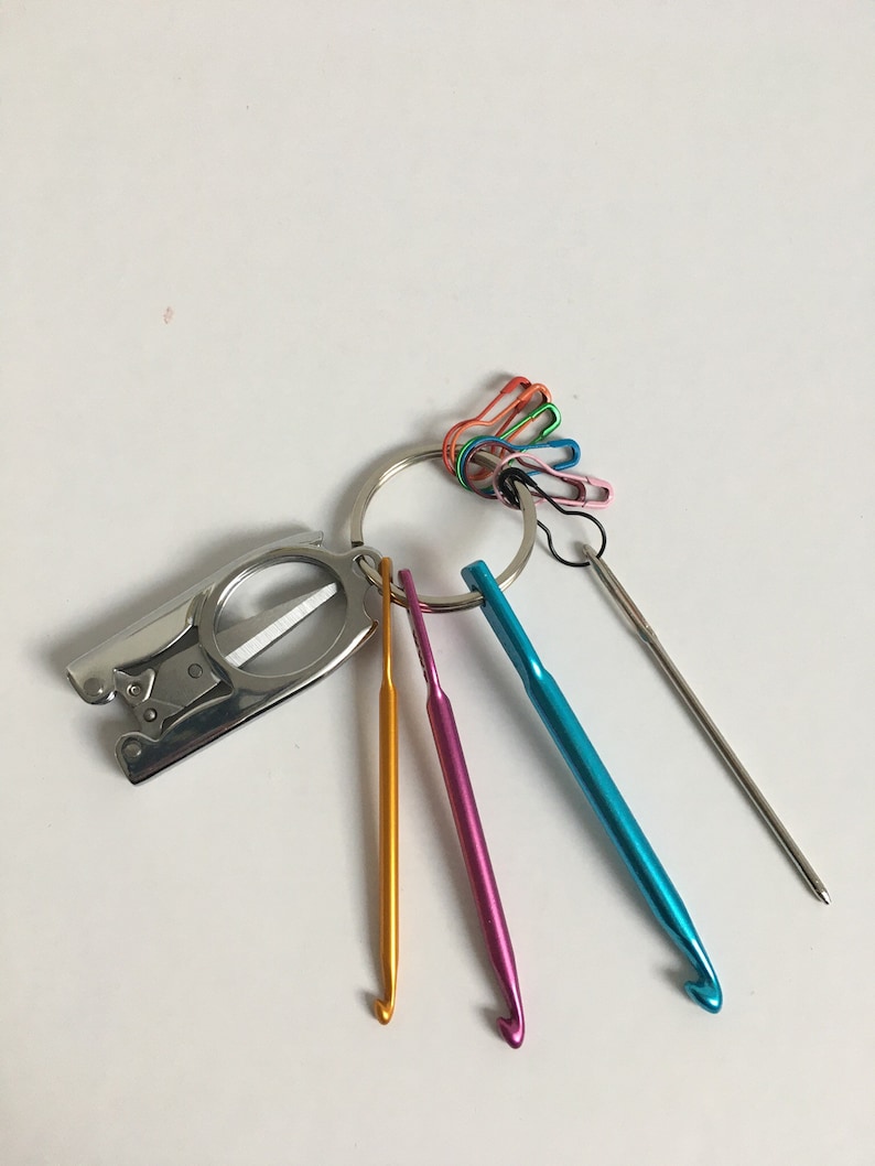 May include: A set of colorful crochet hooks and a small silver tool with a magnifying glass attached to a key ring. The tool also has a small pair of scissors.