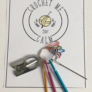 May include: A set of crochet hooks, a pair of scissors, and a set of colorful stitch markers. The set is packaged with a white card with the text "Crochet Me Calm".
