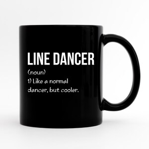 Könnte beinhalten: Eine schwarze Keramiktasse mit dem weißen Text "LINE DANCER", gefolgt von einer Definition. Die Definition lautet: "(Substantiv) 1) Wie ein normaler Tänzer, aber cooler."