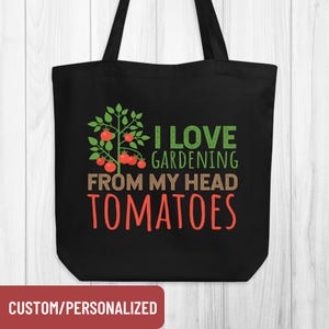 May include: Black tote bag with the text "I LOVE GARDENING FROM MY HEAD TOMATOES" in green, brown, and red. A graphic of a tomato plant is above the text. The bag has black handles and the words "CUSTOM/PERSONALIZED" in a red box at the bottom.