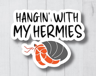 May include: A white sticker with black text that reads "Hangin' with my Hermies". A cartoon hermit crab with an orange body and a grey shell is below the text.