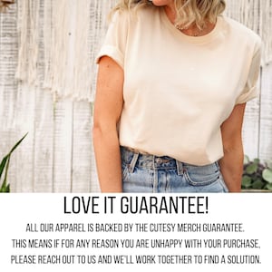 A woman wearing a white t-shirt and blue jeans stands in front of a white wall with a plant.