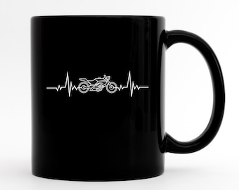 May include: Black ceramic coffee mug with a white motorcycle graphic and a heartbeat line. The mug has a white interior and a black handle.