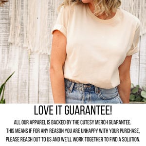 A woman wearing a white t-shirt and blue jeans stands in front of a white wall with a plant.