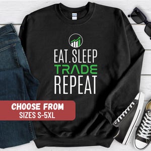 May include: Black sweatshirt with white text that reads "Eat. Sleep. Trade. Repeat." and a green graphic of an upward arrow. The sweatshirt is available in sizes S-5XL.