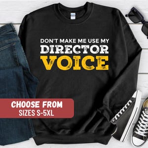May include: Black sweatshirt with the text "Don't make me use my Director Voice" in yellow. The text has a distressed look. The sweatshirt is available in sizes S-5XL.