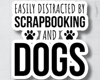 May include: White sticker with black text that reads "Easily distracted by scrapbooking and dogs".  Two paw prints are on either side of the word "and".