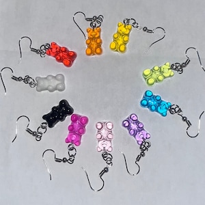 May include: Ten pairs of gummy bear earrings in various colours, including pink, purple, blue, green, yellow, orange, red, white, and black. Each earring features a small gummy bear charm attached to a silver hook.