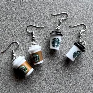 May include: Four pairs of silver dangle earrings with a miniature Starbucks coffee cup charm. The cups are white with a brown lid and a green Starbucks logo.