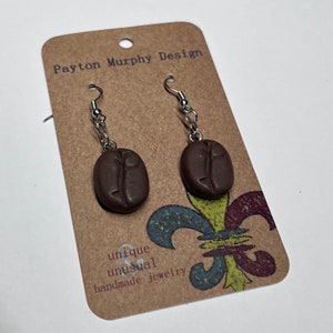 May include: A pair of brown coffee bean shaped earrings with silver hooks. The earrings are on a brown card with the text "Payton Murphy Design" and "unique unusual handmade jewellery".