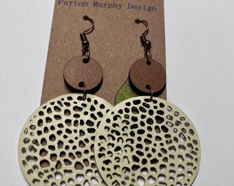 May include: A pair of cream-colored earrings with a cutout design. The earrings are made of leather and have a brown wooden backing. The earrings are hanging from a brown card with the text "Payton Murphy Design".
