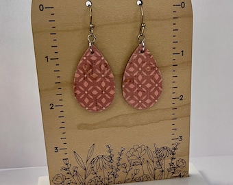 May include: A pair of pink teardrop-shaped earrings with a geometric pattern. The earrings are made of cork and have silver hooks.