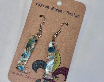 May include: Handmade earrings with a rectangular design. The earrings feature a mix of blue, brown, and white colors. The earrings are displayed on a brown card with the text "Payton Murphy Design" and "unique unusual handmade jewelry".