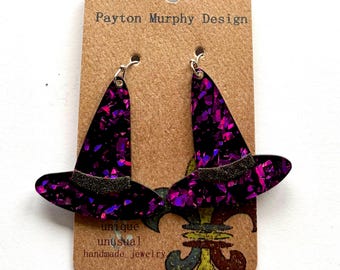 May include: A pair of black witch hat earrings with purple and pink glitter accents. The earrings are on a brown card with the text "Payton Murphy Design" and "unique unusual handmade jewelry".