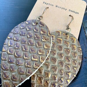 May include: A pair of oval-shaped earrings with a textured, scale-like pattern in shades of brown and gold. The earrings are suspended from bronze-colored ear wires. The earrings are displayed on a brown card with the text "Payton Murphy Design".