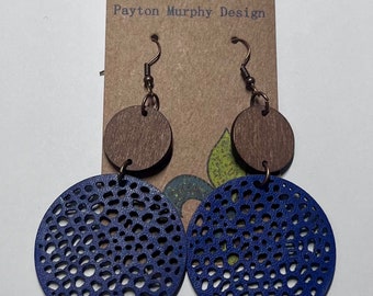 May include: A pair of blue and brown wooden earrings with a cutout design. The earrings are hanging from a brown card with the text "Payton Murphy Design".