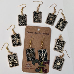 May include: Gold tone earrings with black card-shaped charms featuring tarot card imagery. The cards include The Lovers, The Magician, The Chariot, The World, The Tower, The Star, The Sun, The Moon, The Strength, Death, and Judgement. The earrings are handmade and unique.