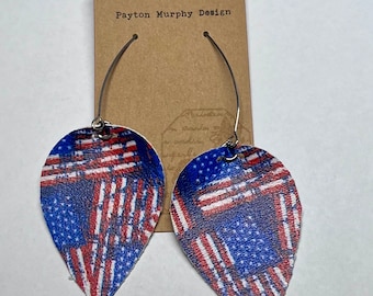 May include: A pair of dangle earrings with a teardrop-shaped leather charm featuring a red, white, and blue American flag pattern. The earrings are made with silver-toned metal.