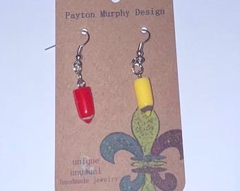 May include: A pair of handmade earrings shaped like pencils, one red and one yellow, on a brown card. The card reads "Payton Murphy Design" and "unique unusual handmade jewelry."