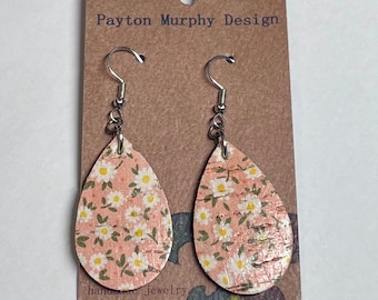 May include: A pair of teardrop-shaped earrings with a pink and white floral pattern on a cork background. The earrings have silver hooks.