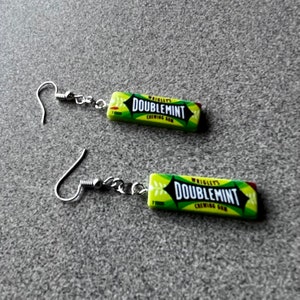 May include: A pair of silver earrings with a green and white Doublemint chewing gum charm. The charm features the text "WRIGLEY'S DOUBLEDMINT CHEWING GUM".