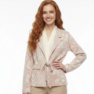 May include: A woman's outfit comprising a pale pink blazer with a white floral design, a cream blouse, and beige trousers. The blazer is belted. The outfit is completed with beige heels.