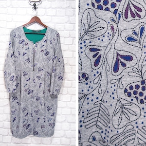Könnte beinhalten: Ein graues, langärmliges Kleid mit Reißverschluss. Das Kleid hat ein Blumenmuster mit violetten und blauen Akzenten. Das Muster erinnert an stilisierte Blätter und Blumen.