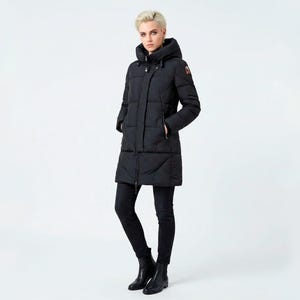 Puede incluir: Un abrigo largo negro acolchado con capucha. El abrigo tiene un diseño acolchado y cierre de cremallera. La modelo lleva pantalones negros y botas negras. El fondo es blanco.