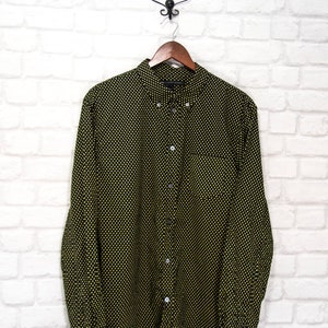 May include: A black and yellow patterned long-sleeved button-down shirt hanging on a wooden hanger against a white brick wall.