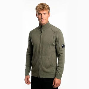 May include: A white ceramic mug with a black handle and the text "But First, Coffee" in a bold, black font. The mug is set against a blurred background, suggesting a cozy setting.