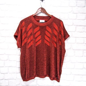 May include: A red sparkly short-sleeved sweater with a geometric pattern. The sweater has a round neckline and is made of a soft, comfortable material.