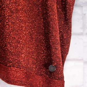 May include: A red sparkly fabric with a small, round, black tag with a design on it.