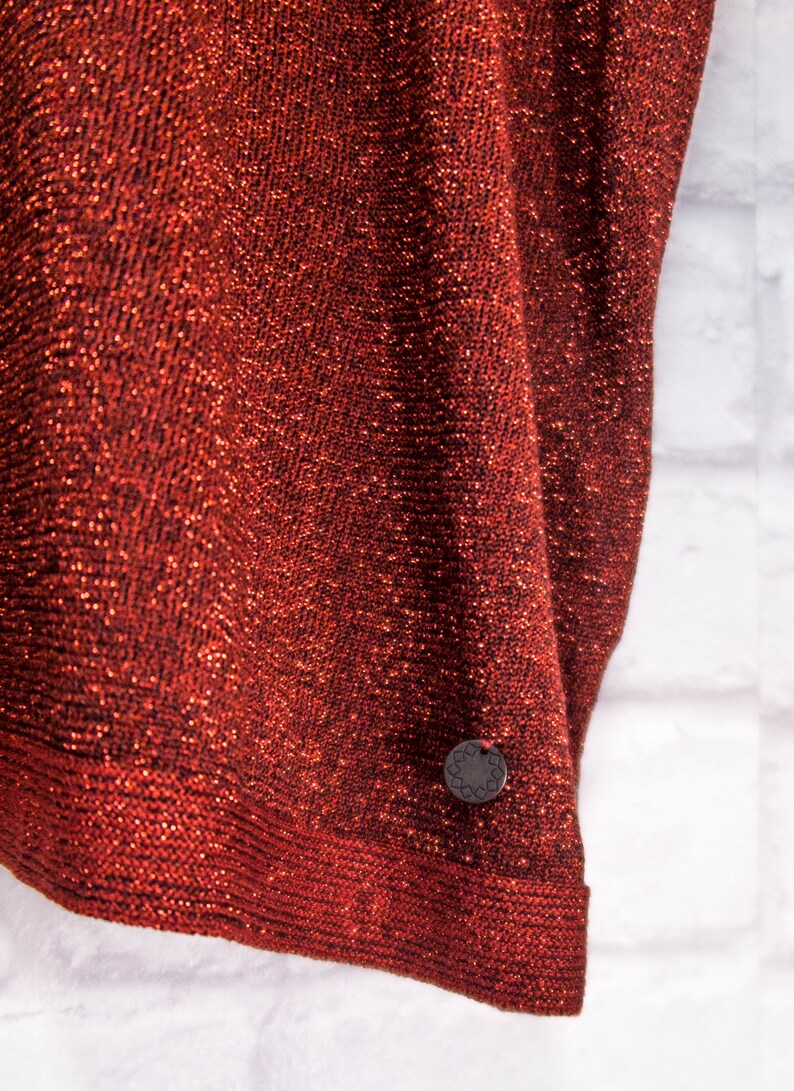 May include: A red sparkly fabric with a small, round, black tag with a design on it.