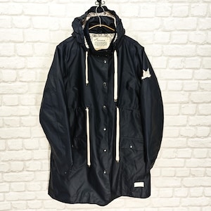 May include: A navy blue hooded jacket with a drawstring waist and white drawstrings. The jacket has a button-up front, two front pockets, and a small white label. A white emblem is on the right sleeve. The jacket is hanging on a decorative hook.
