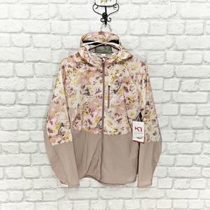 Könnte beinhalten: Kapuzenjacke mit Reißverschluss und floralem Muster in Rosa, Gelb und Weiß. Der untere Teil ist mauvefarben. Ein Etikett mit Logo ist angebracht. Die Maße der Jacke sind in Zentimetern.