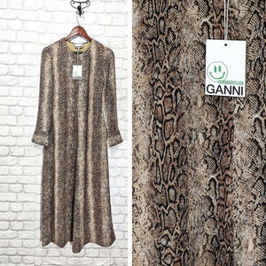 May include: A long-sleeved maxi dress with a brown and black snake print. The dress has a round neckline and a relaxed fit. The dress is made by the brand GANNI.