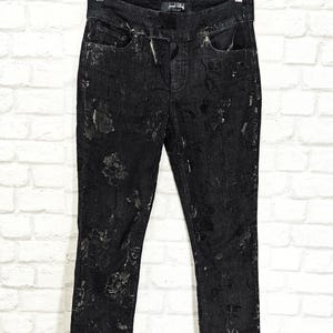 May include: Black denim jeans with a floral pattern in silver. The jeans have a high waist and a slim fit.