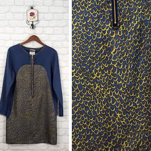 May include: A blue and yellow patterned tunic with a zipper up the front. The tunic has long sleeves and a round neckline.