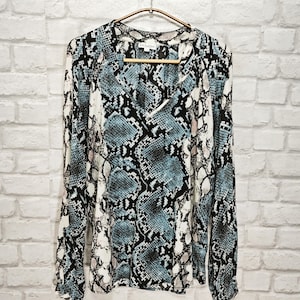 Peut inclure: Un chemisier à manches longues avec un imprimé serpent dans les tons de bleu, noir et blanc. Le chemisier a un col en V et une coupe ample.