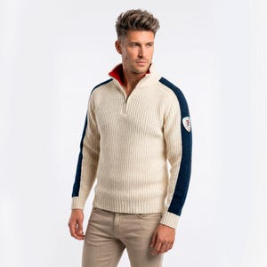 May include: Cream-colored, ribbed knit sweater with a navy blue stripe down the sleeves and a red collar. The sweater has a quarter-zip closure and a small emblem on the upper arm. The model is wearing khaki pants.