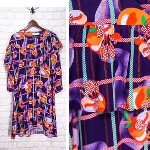 May include: A purple and orange patterned dress with a ruffled neckline and long sleeves. The dress has a geometric pattern with orange and green accents.