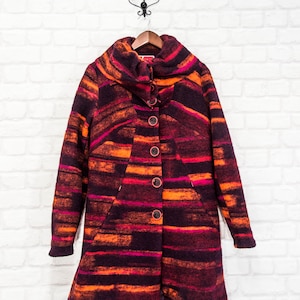 Peut inclure: Un manteau à manches longues, rayé, avec un col montant et une fermeture à boutons. Le manteau est fait d'un tissu doux et duveteux et présente un motif abstrait coloré dans les tons orange, rose et violet.