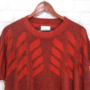 May include: A red short-sleeved sweater with a geometric pattern. The sweater is made of a sparkly material.