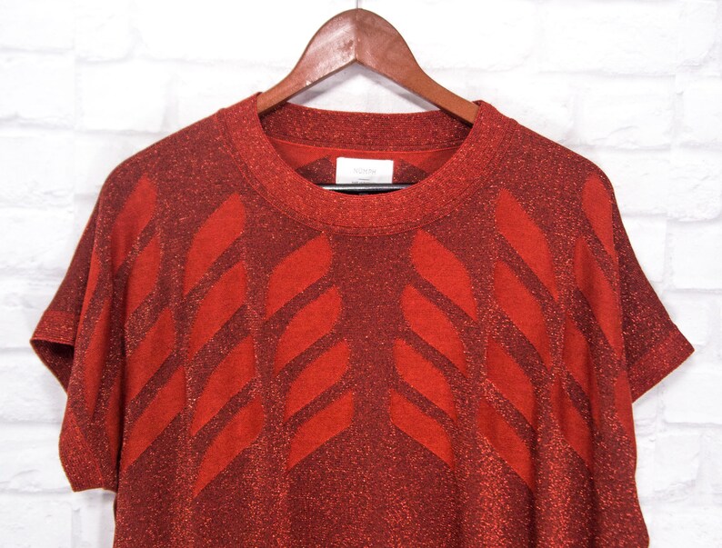 May include: A red short-sleeved sweater with a geometric pattern. The sweater is made of a sparkly material.
